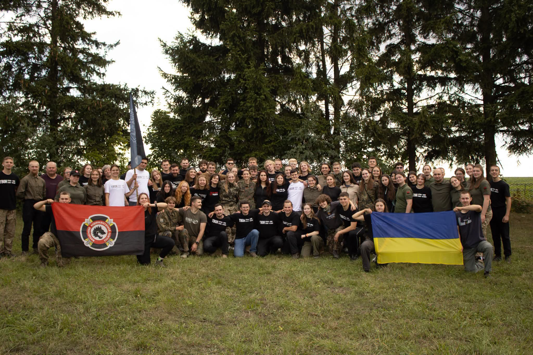 Учасники гри зібралися на спільному фото на галявині серед ялин. У руках тримають червоно-чорний прапор і державний прапор України.