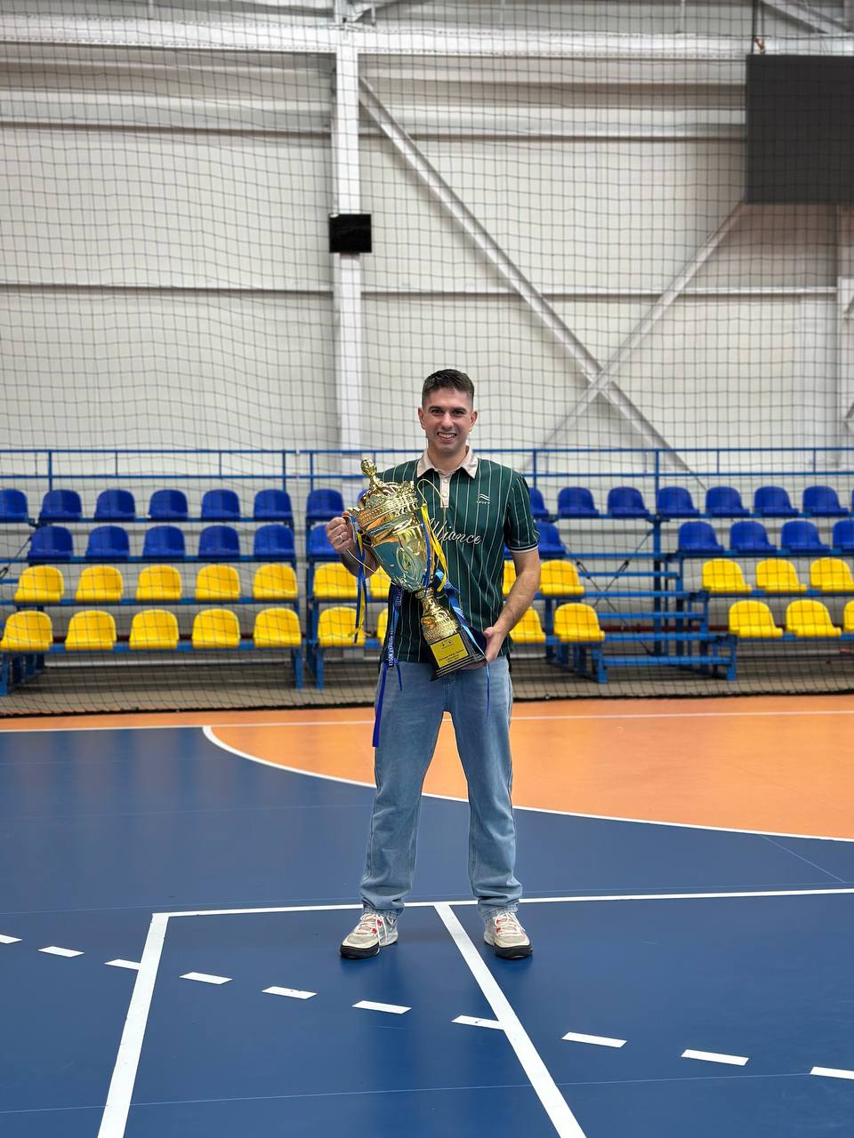 Тренер Максим Антоневич стоїть на полі та тримає великий золотий кубок Кубка України. Він усміхається в камеру.